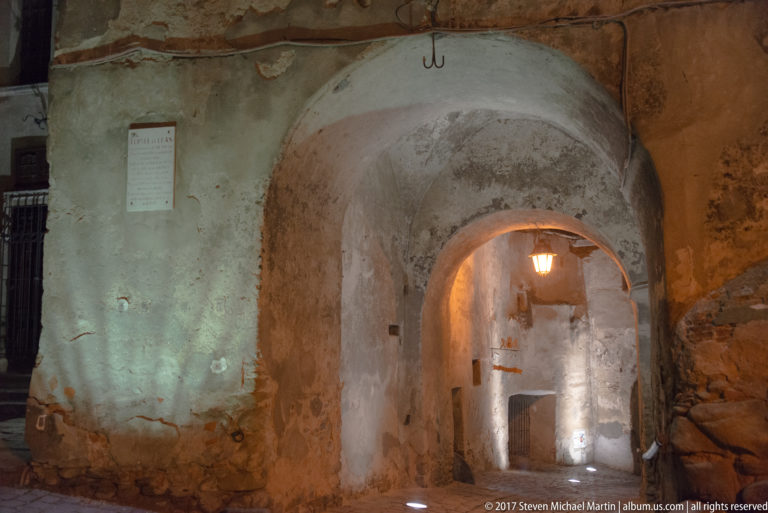 Weathered plaster and stone arches form a dimly lit passage with a hanging lamp.