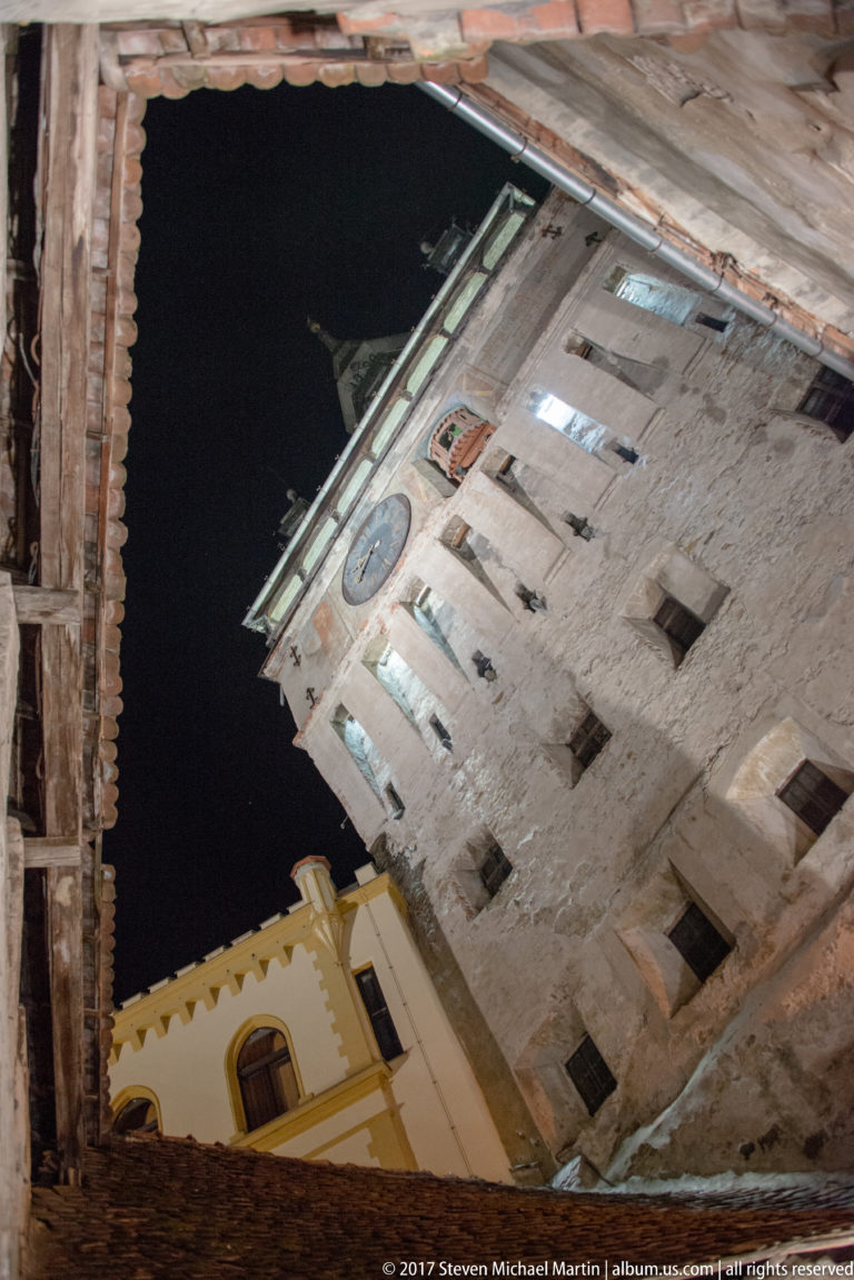 Tilted low-angle view up Sighisoara Clock Tower, showing its clock face, masonry wall, and roofline.