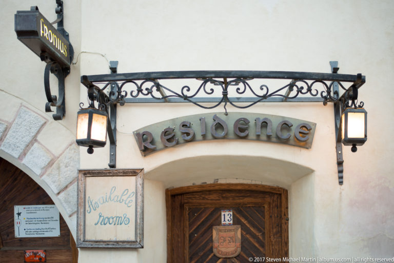 Wooden doorway beneath a wrought-iron “Residence” sign, flanked by lanterns, an available-rooms notice, and number 13.