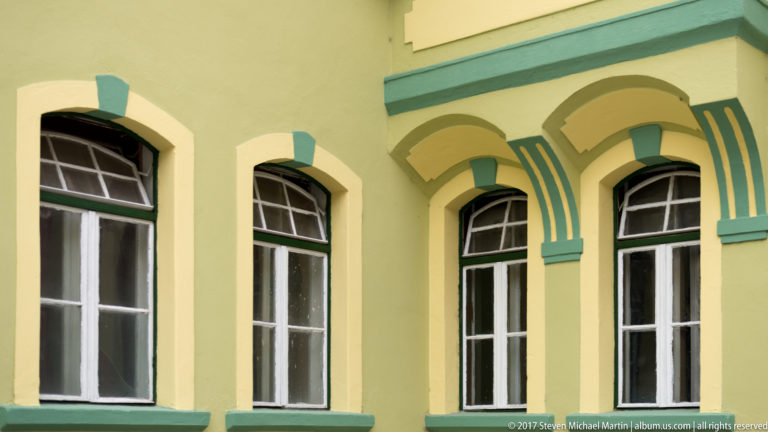 Tall arched windows on a pale yellow façade with green pilasters, molded arches, and cream decorative bands.