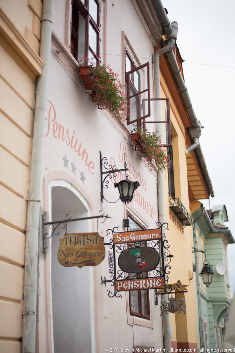 Pale guesthouse façade with wrought-iron Pensiune and San Gennaro signs, flower boxes, windows, and painted lettering.
