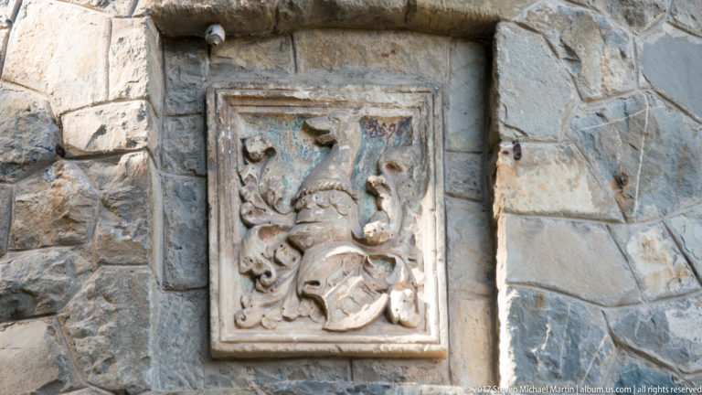 Rectangular carved relief with scrolling forms and a shield-like central motif is inset into irregular gray stone masonry