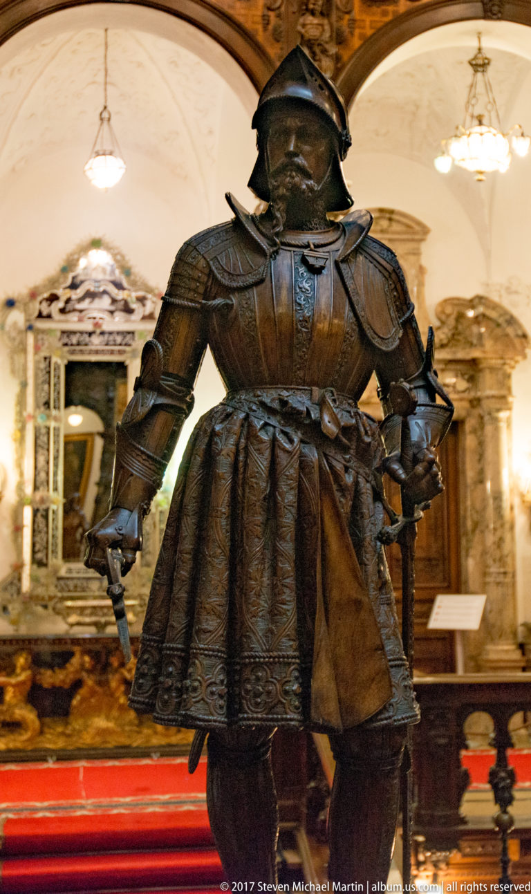 Dark full suit of plate armor with closed helmet, broad shoulders, articulated arms, and flared ridged lower plates.