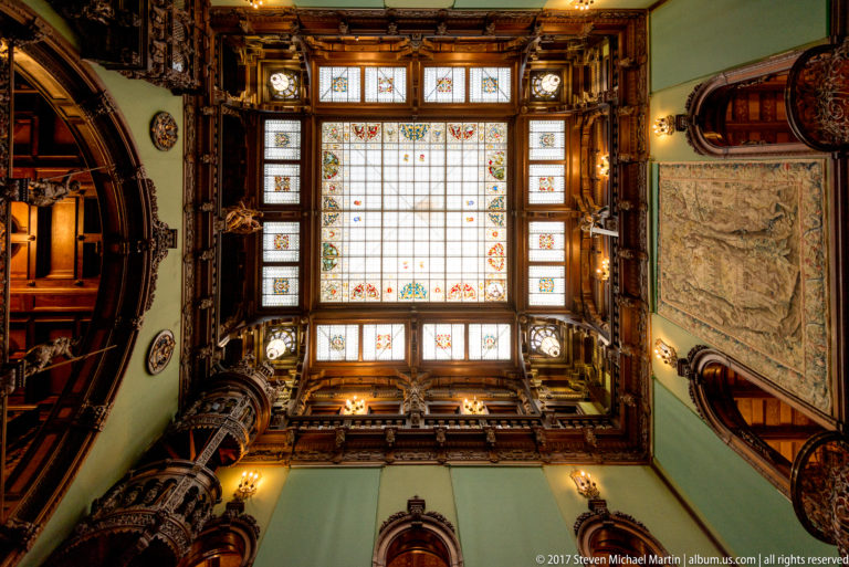 Rectangular leaded-glass skylight with small colored motifs, framed on all sides by carved wooden galleries and ornament.