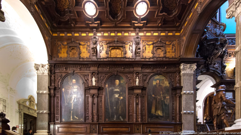 Three tall portraits set into dark carved wood paneling with columns, relief ornament, and decorative friezes.