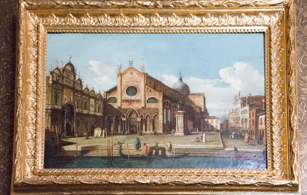 Gilded framed painting of a Venetian church, waterfront, small figures, and surrounding historic buildings.