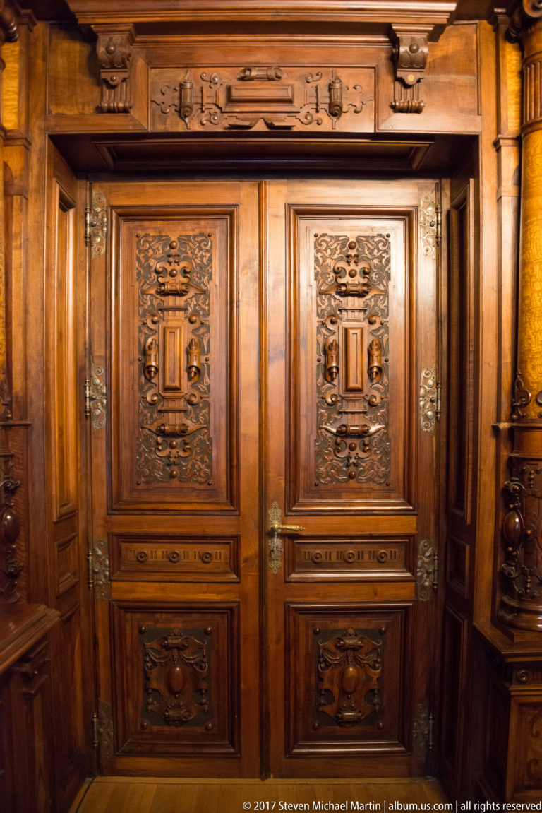 Pair of richly carved wooden doors with symmetrical panels, metal handles, and an ornate carved surround.