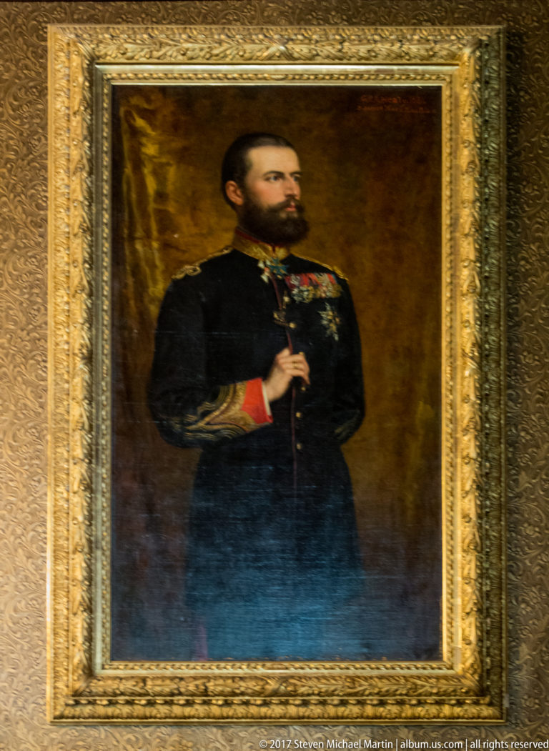 Framed oil portrait of a bearded man in dark formal military dress with decorations and a red cuff.