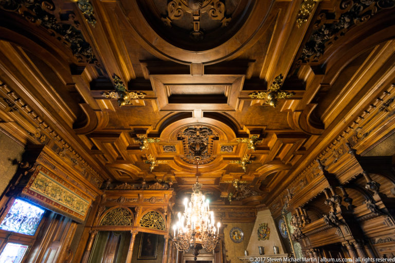 Deeply carved geometric wooden ceiling with gilded accents and a crystal chandelier hanging from the center.