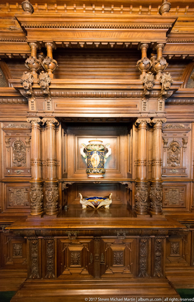 Large carved wooden sideboard with cupboards, fluted columns, relief panels, and a decorative vessel in the central niche.