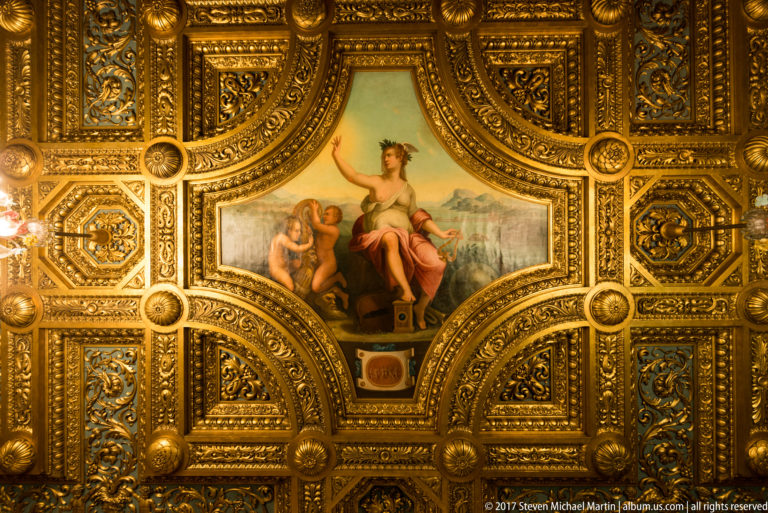 Figural painted panel surrounded by elaborate gilded coffers, rosettes, and carved geometric ornament.