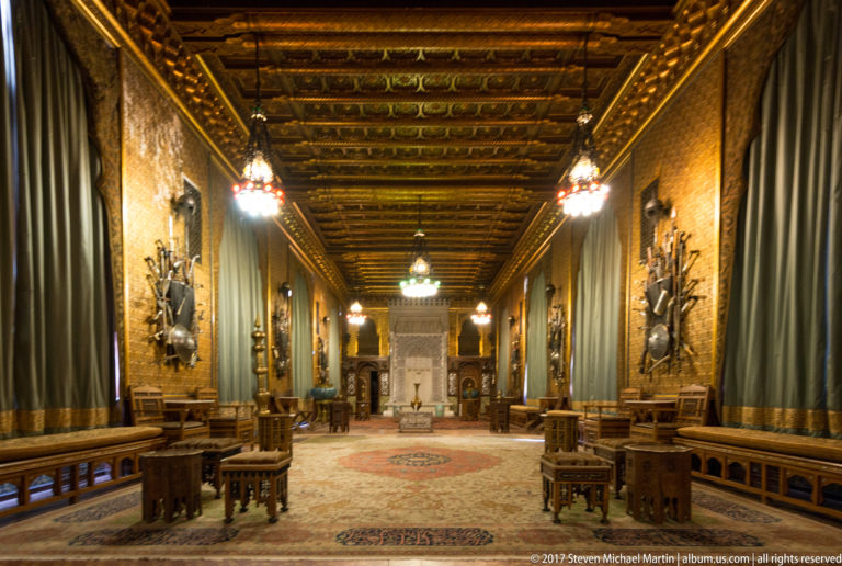 Long wood-paneled ceremonial hall with benches, arms displays, hanging lights, and an ornate coffered ceiling.