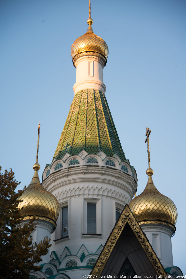 Golden onion domes and patterned green roof of Sofia’s Russian Church, each topped by Orthodox crosses.