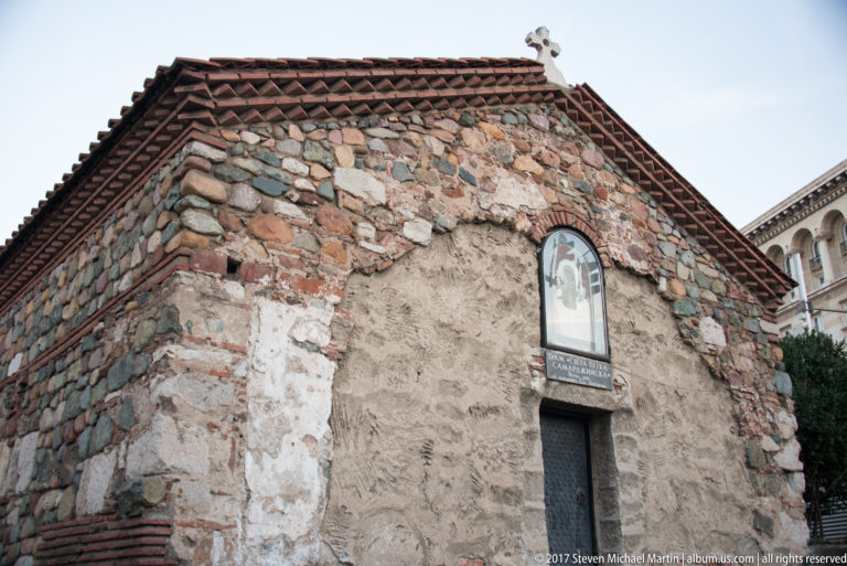 Rough stone-and-brick wall of the small Church of St. Petka of the Saddlers, with tiled roof and religious plaque.