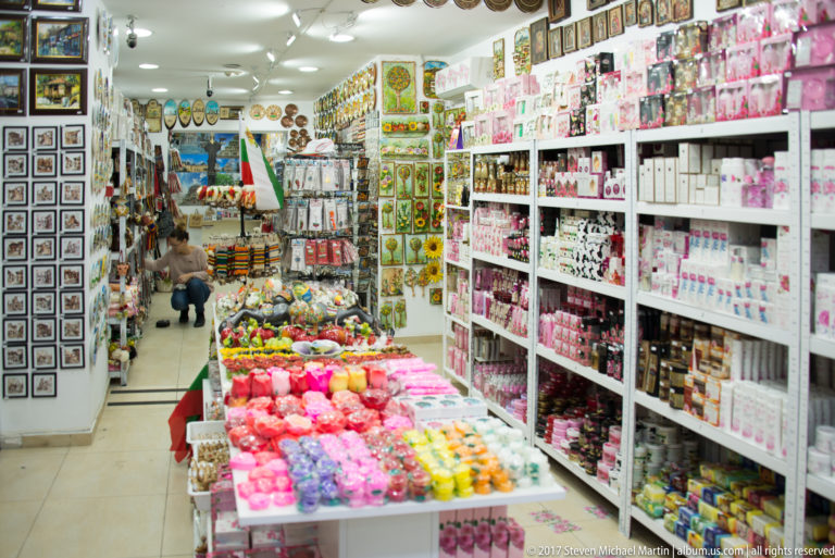 Narrow Sofia souvenir shop packed with postcards, gifts, cosmetics, and colorful merchandise on tables, shelves, and wall racks.