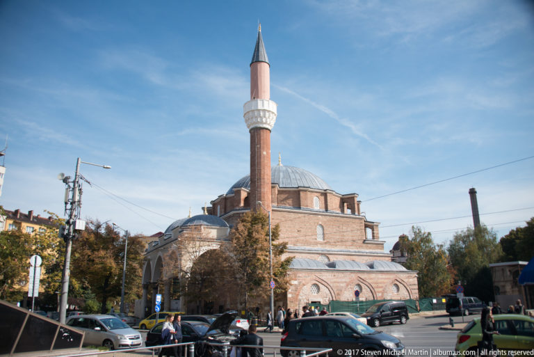 Banya Bashi Mosque with domed prayer hall and tall minaret beside a busy Sofia street.