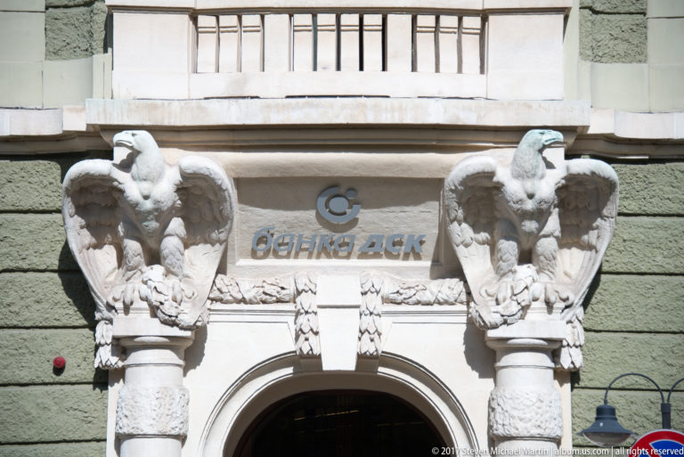Two sculpted eagles on columns flank an arched doorway with Cyrillic signage on a Sofia building.