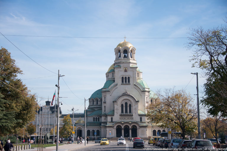 Alexander Nevsky Cathedral centered at the end of a city street lined with trees, flags, and traffic.