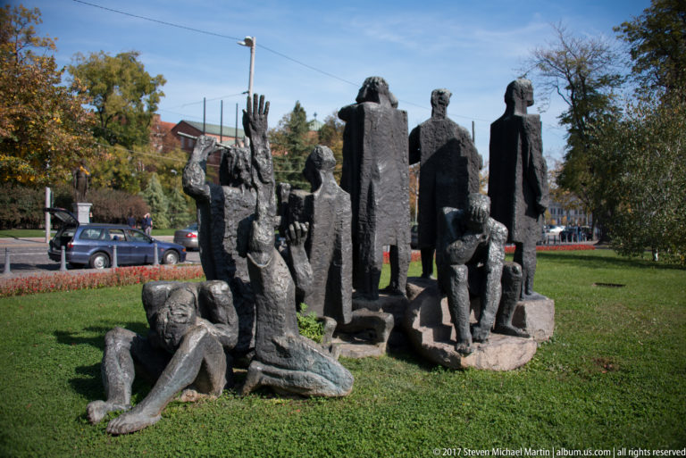 Bronze group of standing and seated human figures on grass in a landscaped urban park in Sofia.