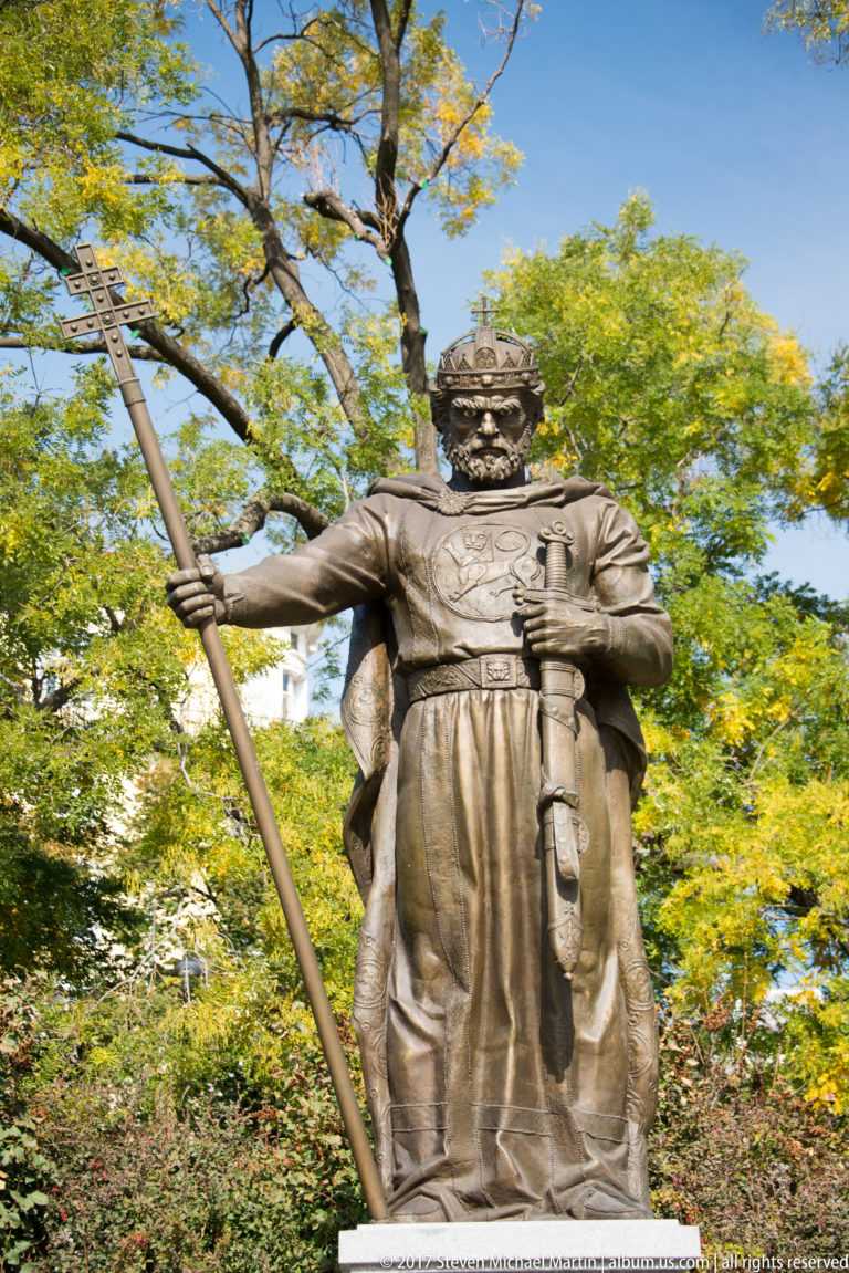 Bronze statue of a medieval warrior or ruler holding a long spear and sword among trees in Sofia.