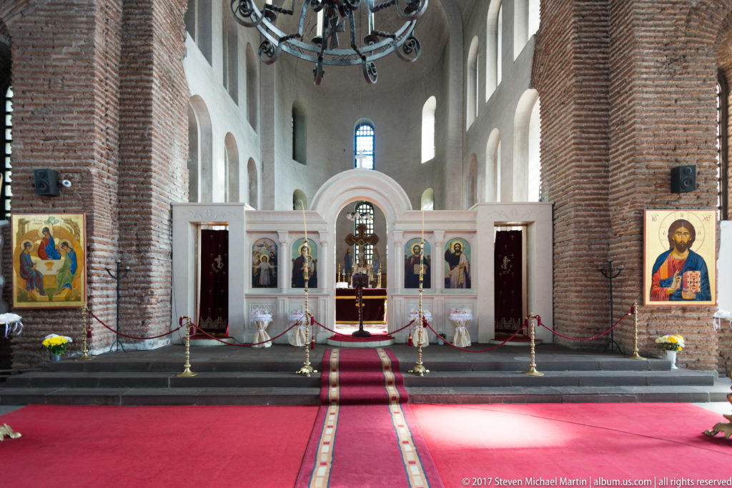 Sanctuary of the Church of Saint Sofia with a white icon screen, red carpet, brick piers, and high windows.