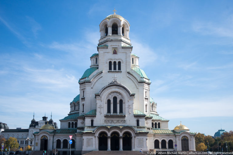 Frontal view of Alexander Nevsky Cathedral with white façade, green roofs, and a gold-topped central tower.