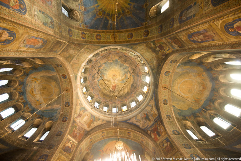 Upward view across several painted domes and vaults with arched windows inside Alexander Nevsky Cathedral.