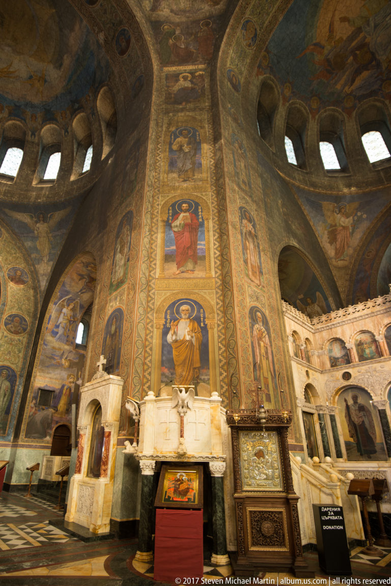 Massive interior pier painted with full-length saints, surrounded by marble furnishings and arches in Alexander Nevsky Cathedral.