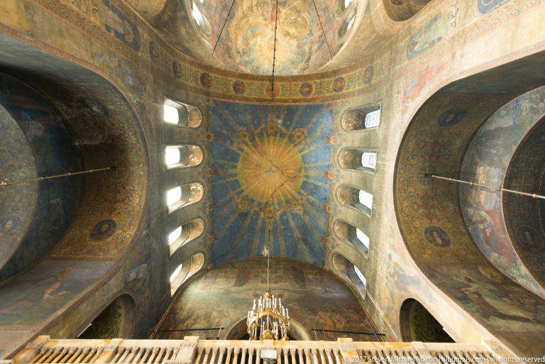 Upward view of painted dome, vaulted ceilings, clerestory windows, and chandelier inside Alexander Nevsky Cathedral.