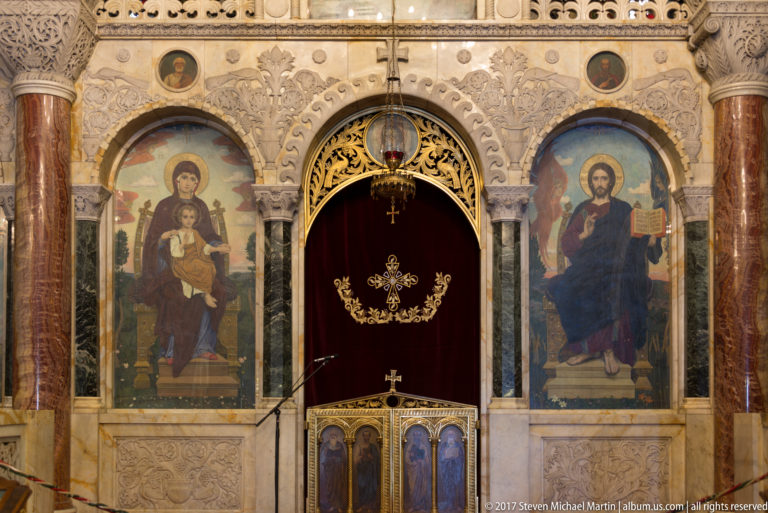 Ornate iconostasis section with large icons of the Virgin and Child and Christ flanking a central curtained opening.