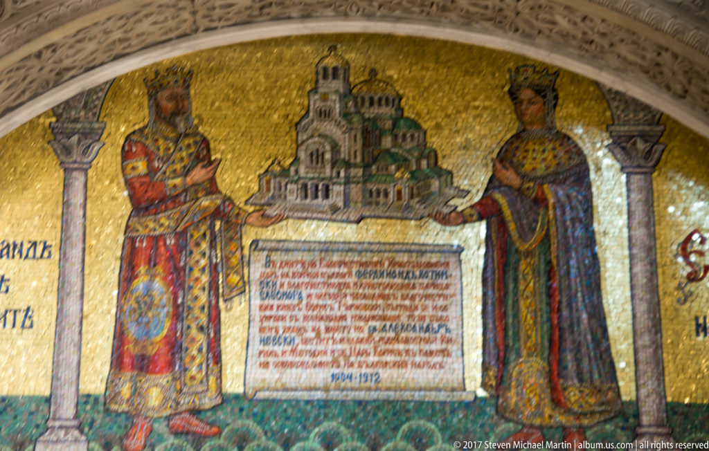 Gold mosaic of two robed rulers beside a model of Alexander Nevsky Cathedral and an inscribed tablet.