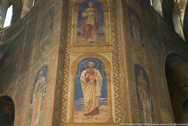Tall fresco panels of haloed saints framed by patterned borders on an interior wall of Alexander Nevsky Cathedral.
