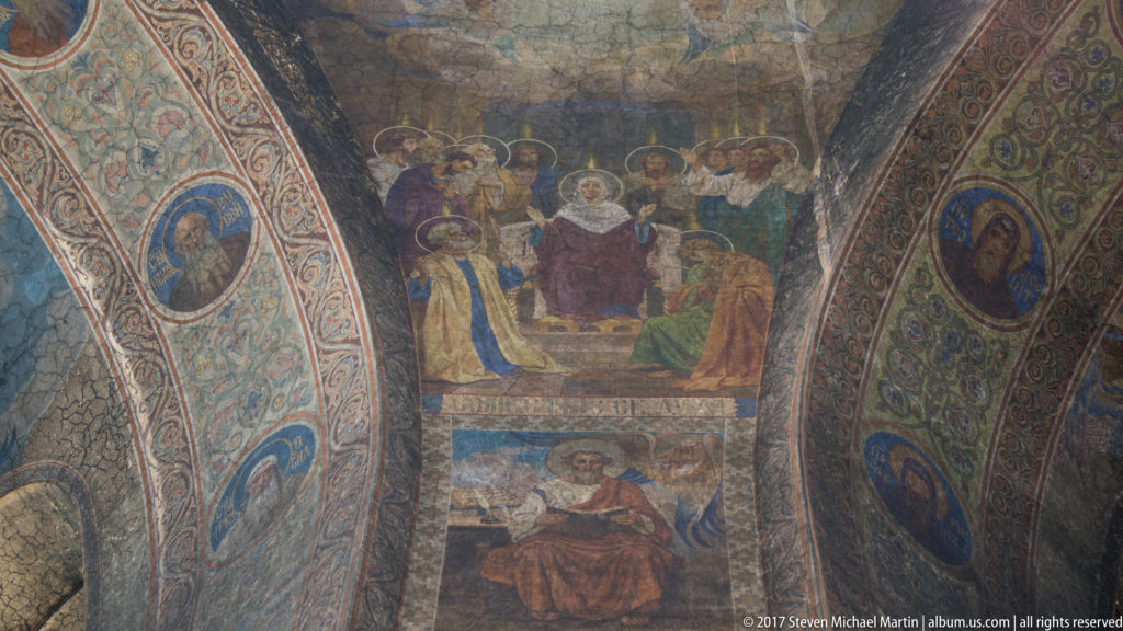 Curved cathedral wall covered with multi-scene Orthodox frescoes, haloed figures, and decorative painted borders.