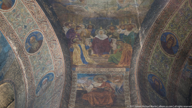 Curved cathedral wall covered with multi-scene Orthodox frescoes, haloed figures, and decorative painted borders.