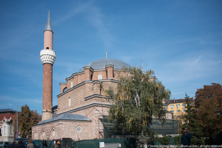 Side view of Banya Bashi Mosque with tall minaret, broad dome, arched windows, and striped masonry.