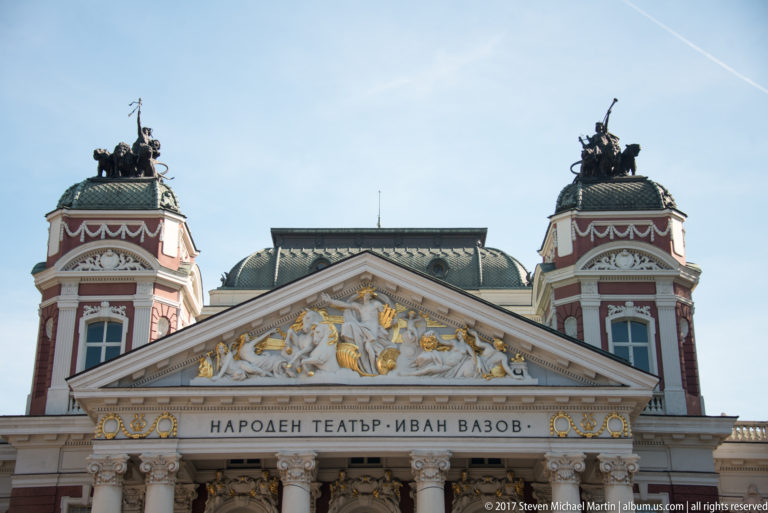 Upper façade of Ivan Vazov National Theatre with twin towers, sculpted pediment, gilded accents, and Bulgarian name inscription.