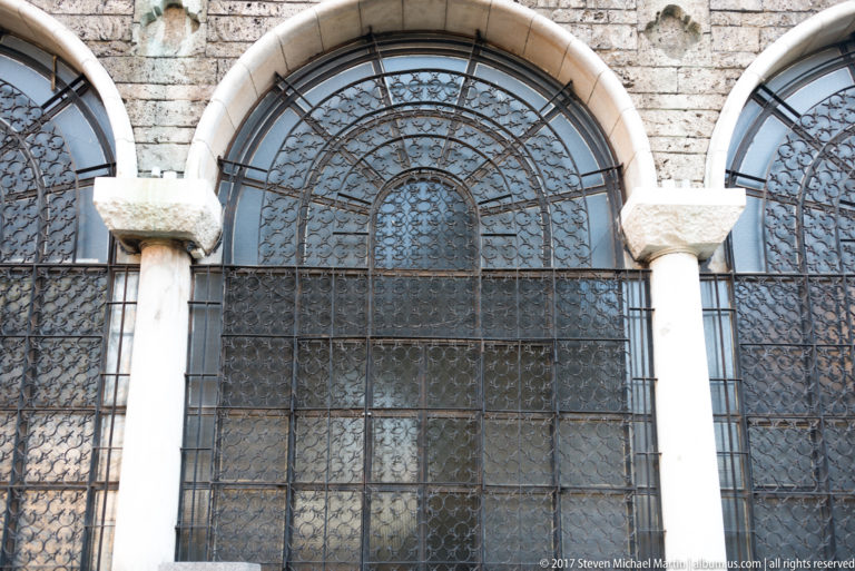 Tall arched windows of Saint Nedelya Church covered by intricate iron grilles and divided by pale stone columns.