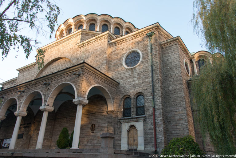 Side view of Saint Nedelya Church with columned arcade, round window, layered masonry walls, and upper clerestory.