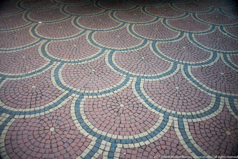 Close view of red, cream, and dark green pavers arranged in repeating fan-shaped patterns.