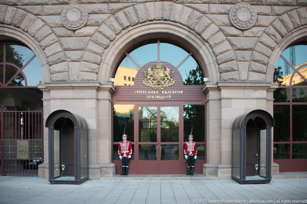Stone-arched entrance to Bulgaria’s presidency with national emblem, Bulgarian inscription, and two ceremonial guards in red uniforms.