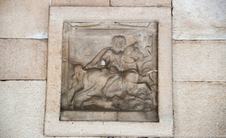 Weathered stone relief of a mounted figure on horseback, mounted within a pale masonry wall.