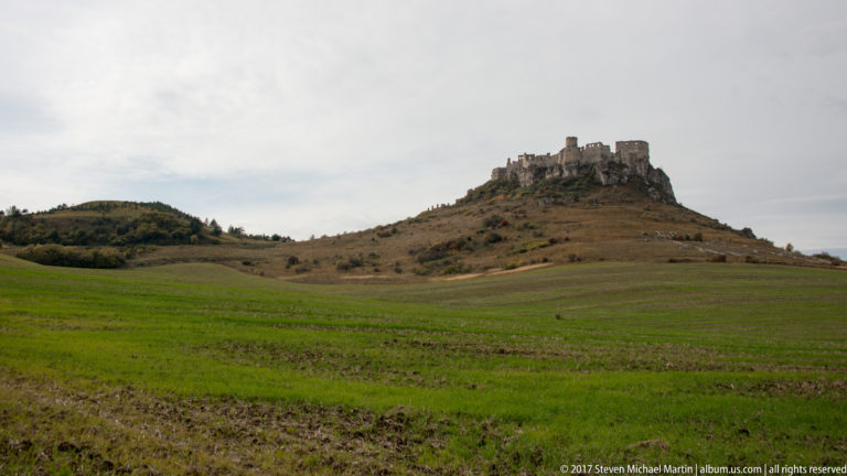 Stone castle ruin on a bare hill above rolling green and brown fields.