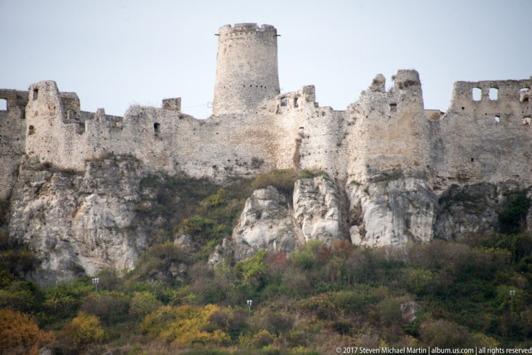Close exterior of ruined stone walls and a cylindrical tower rising from a rocky slope at Spiš Castle.