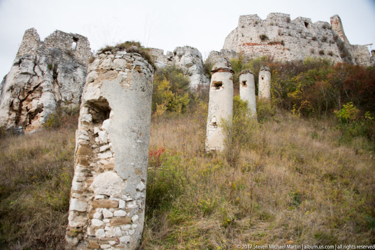 Several narrow weathered masonry remnants in grass below ruined castle walls and exposed rock.
