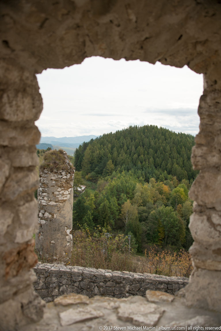 Wooded hillside seen through an irregular opening in thick rough stone masonry inside the castle ruins.