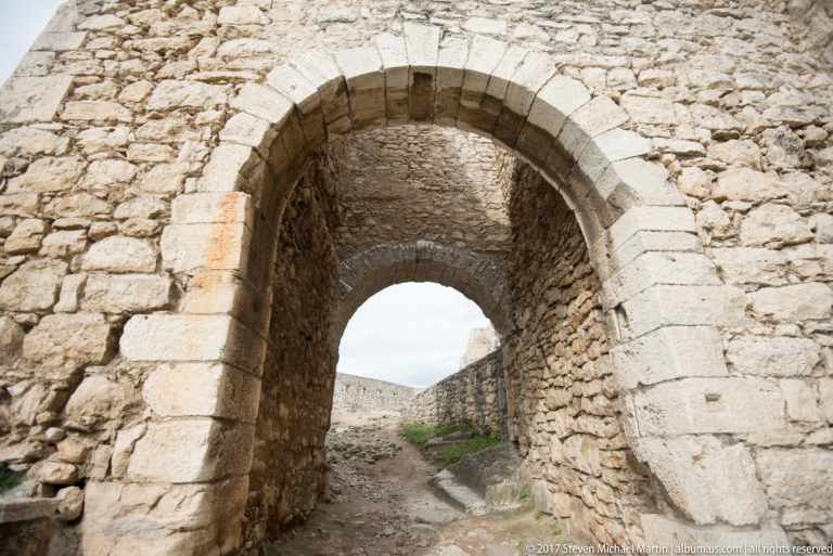 Large round stone arch framing a second arch deeper inside a thick castle passage.