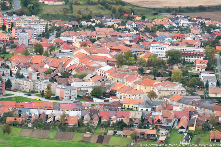 Dense town of red-roofed houses, apartment blocks, streets, and garden plots seen from above.