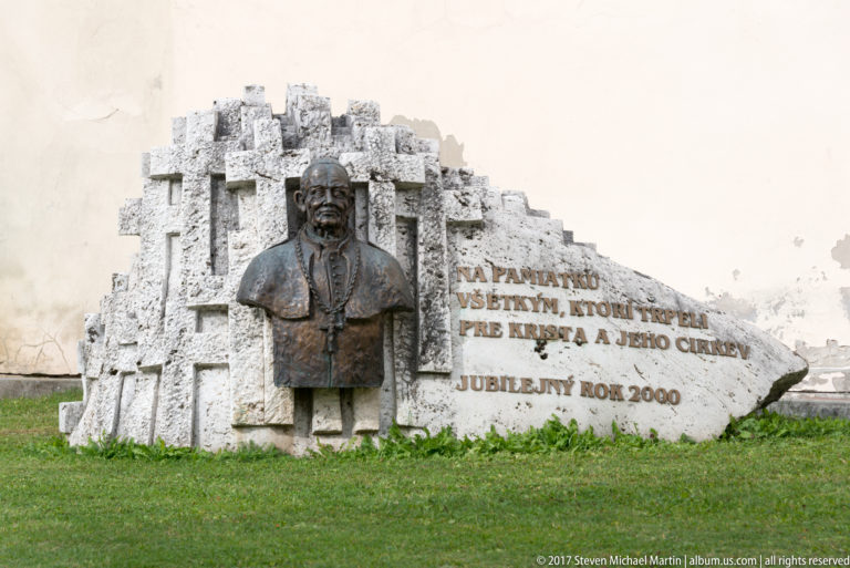 Bronze bust mounted on a pale stone memorial with Slovak inscription and “Jubilejný rok 2000” visible.