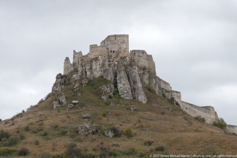 Closer view of Spiš Castle's upper ruins rising from jagged rock on a steep scrub-covered hill.