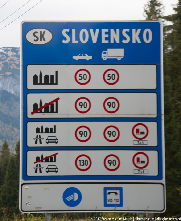 Blue SLOVENSKO border sign displaying Slovak speed limits for several road and vehicle categories.